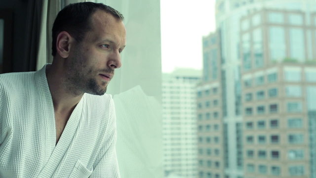 Young sad, pensive man by the window looking at cityscape