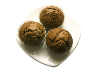 Three gingerbread muffins in cups on a plate.