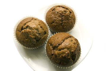 Three gingerbread muffins in cups on a plate.