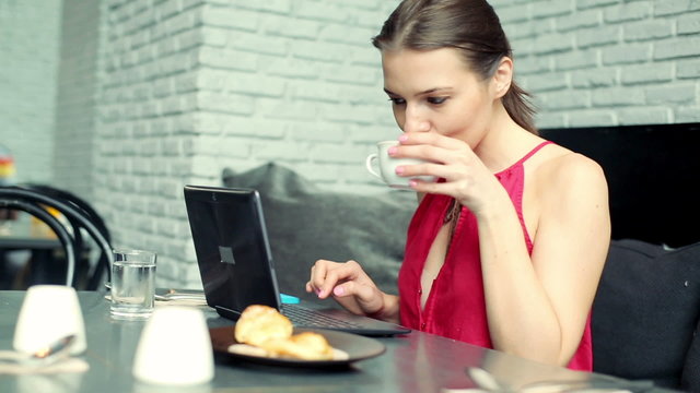 Woman working on modern laptop and drinking coffee in cafe
