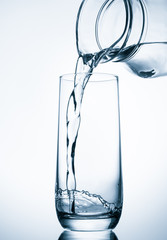 Pouring water from glass pitcher on blue background
