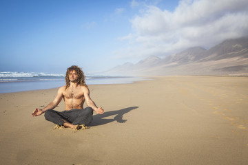 young handsome man doing yoga meditation on the beach
