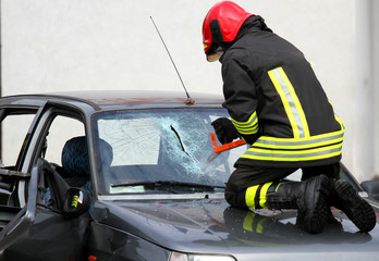 Fototapeta premium Fireman with work gloves while breaking a car windshield to rele
