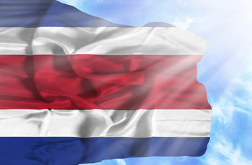 Costa Rica waving flag against blue sky with sunrays