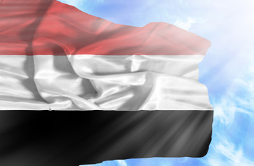 Yemen waving flag against blue sky with sunrays