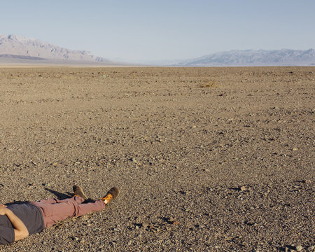 A man lying on his back on the ground in the desert.