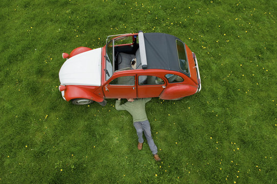 A man lying on his back under a red car, inspecting the underside of the car.