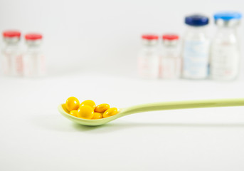 Yellow coating tablet in spoon on vial background