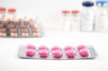 Pink tablet in blister pack on medicine vials background