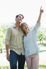 Carefree couple standing in the park with woman pointing