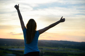 happy young woman outdoor rising hands and looking at sunset