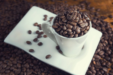 Close up of a white cup full of coffee beans, on a wooden table.
