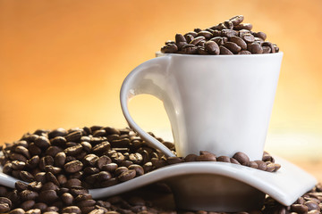 White cup full of coffee beans, over shiny yellow background.