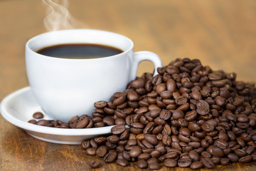 Cup of coffee,surrounded with coffee beans,on a wooden table.