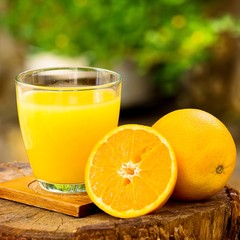 Fresh orange juice in a glass, outside, on the stump.