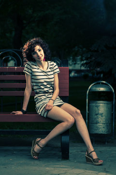 A beautiful girl is sitting on a park bench on a background of g
