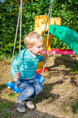 Cute little blond boy swinging on swings outdoor playground