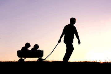 Silhouette of Father Pulling Sons in Wagon at Sunset