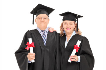 Mature couple in graduation gowns with diplomas