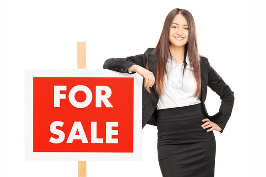 Female realtor leaning on a for sale sign
