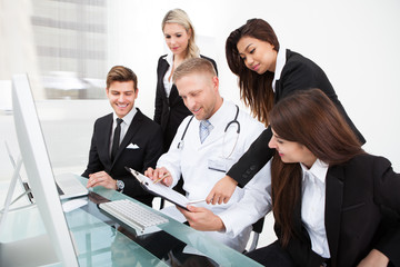 Doctor And Businesspeople Discussing Over Clipboard