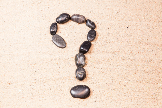 question mark drawn with pebbles on the sand of a beach