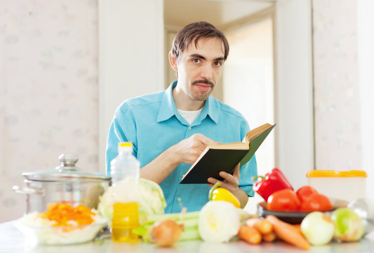 handsome  man cooking  vegetables with cookbook