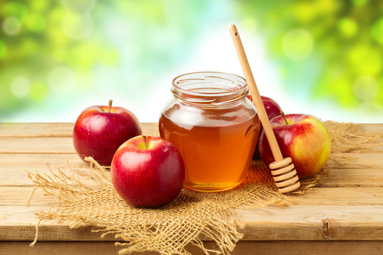 Honey and apples on wooden table over bokeh background