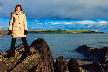 Woman standing on rock cliff at ocean, relaxing Co. Cork Ireland