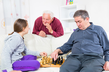 portrait of a girl and grandfather playing chess at home
