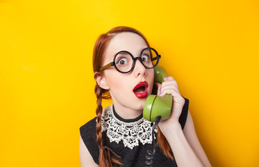 Redhead girl with green phone on yellow background.