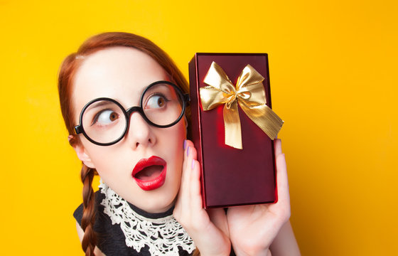 Redhead girl with gift on yellow background.