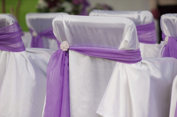beautiful white wedding chairs decorated with purple bows