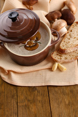 Mushroom soup in pot, on wooden background