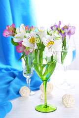 Freesias in glasses on table on fabric background