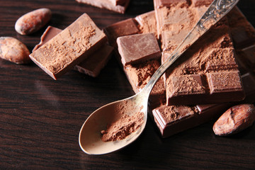 Cocoa powder and dark chocolate on color wooden background