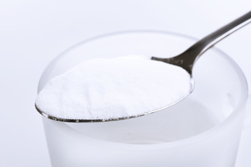Spoon of baking soda over glass of water, isolated on white