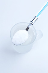 Spoon of baking soda over glass of water, isolated on white