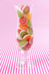 Different colorful fruit candy in glass on pink background