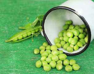 Fresh green peas in metal cup on wooden table