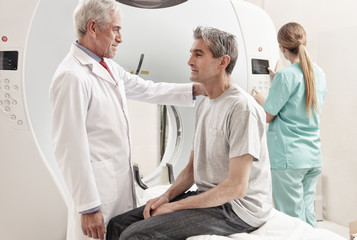 Obraz premium Senior male doctor explaining CT scanner exam to man in 40s. Fem