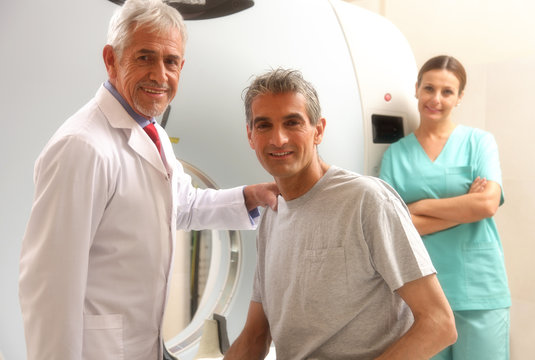 Happy Senior Doctor With His Male Patient At CT Scanner Machine.