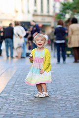 Cute little girl eating ice-cream in the center of crowed street
