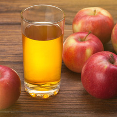 Glass of apple juice and red apples on wood
