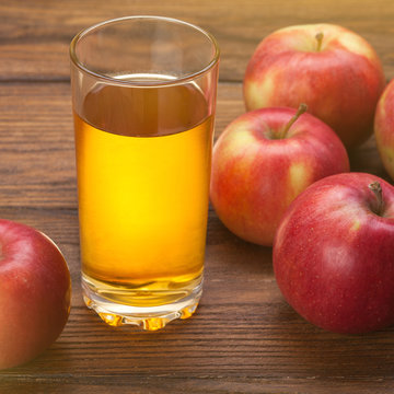 Glass of apple juice and red apples on wood