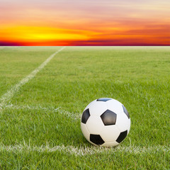 Naklejka premium soccer ball on soccer field against sunset sky