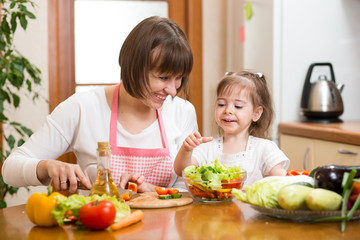 Young woman and her child daughter making vegetable salad