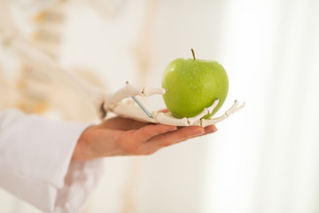 Closeup on doctor woman with human skeleton hand holding apple