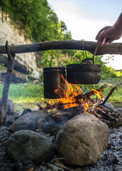 Man stirs ladle food that is prepared in a hike in the cauldrons