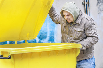 Fototapeta na wymiar Homeless near yellow garbage container